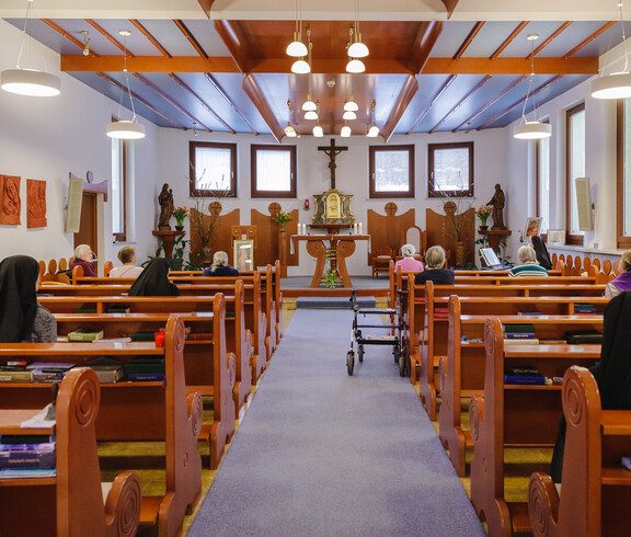 Einige Schulschwestern sowie Bewohner*innen sitzen in der hauseigenen Kappele und sehen zum Altar.