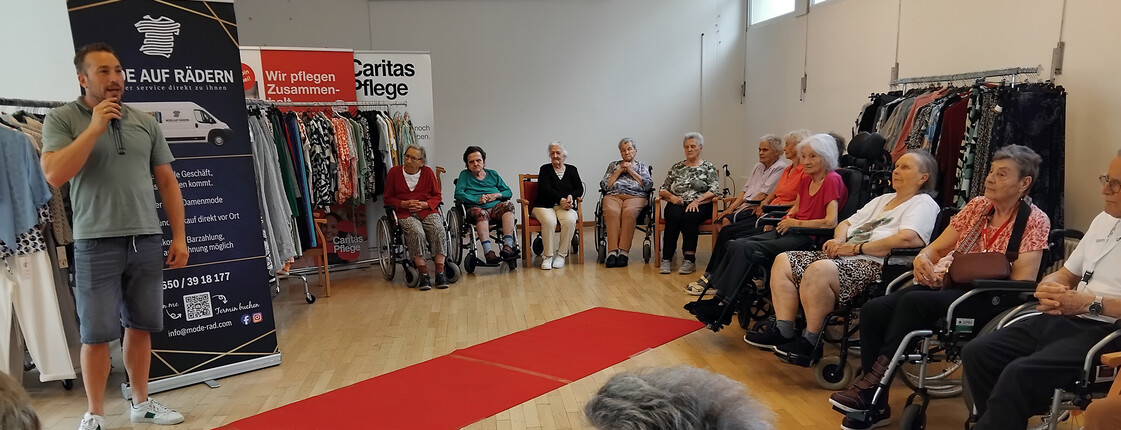 Publikum verfolgt die Modenschau im Saal des St. Hemma Hauses zwischen Kleiderständern.