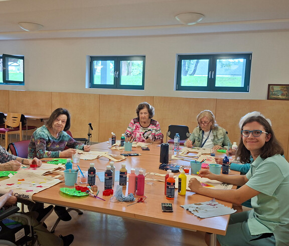 Bewohner*innen und Mitarbeitende gestalten Stofftaschen mit Farben beim kreativen Workshop im Haus Magdalena.