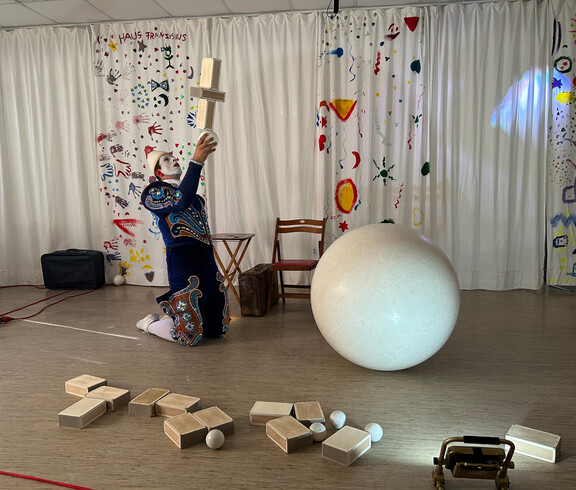Weißclown balanciert Holzklötze und Ball auf der Bühne bei einer Zirkusvorführung in Haus Franziskus.