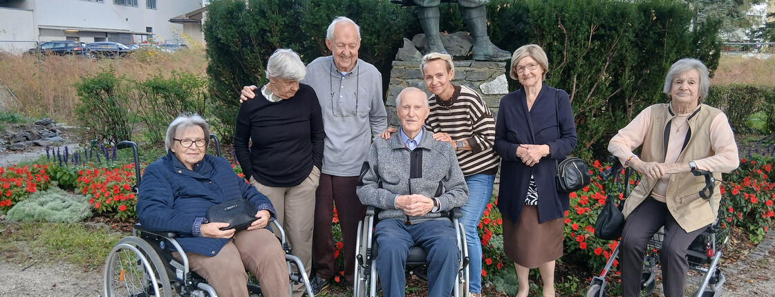 Sieben ältere Personen und eine Begleitperson versammeln sich bei einem Ausflug für ein gemeinsames Gruppenbild im Freien.