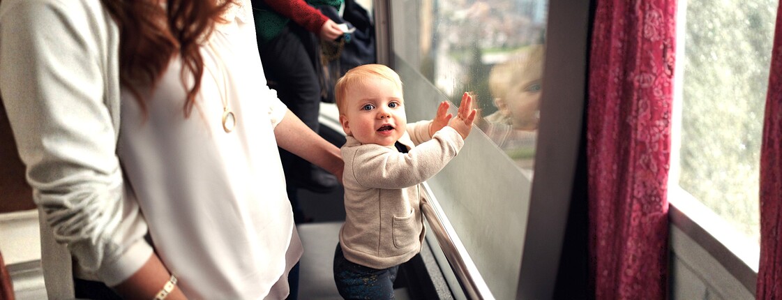 Ein kleines Kind steht an einem Fenster und wird von einer Frau gestützt