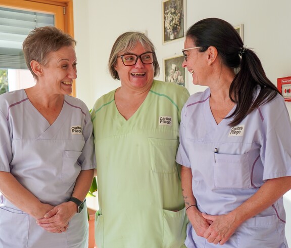 Drei Pflegerinnen stehen neben einander und lachen.