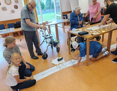 Kinder und Senior*innen programmieren gemeinsam einen Mini-Roboter auf Papierstrecke im Festsaal