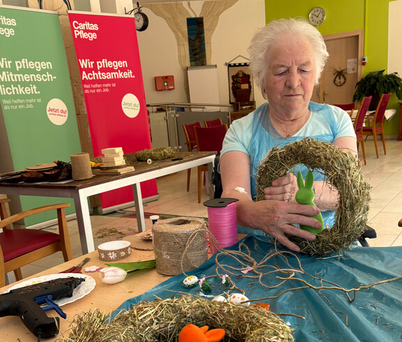 Bewohner*in hält einen selbst gestalteten Osterkranz aus Naturmaterialien am Basteltisch.