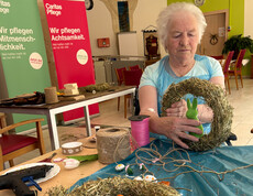 Bewohner*in hält einen selbst gestalteten Osterkranz aus Naturmaterialien am Basteltisch.