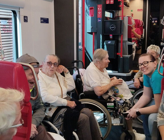 Senior*innen mit Betreuer*innen sitzen in einem Zug, teils im Rollstuhl, teils auf Sitzen