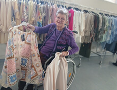 Bewohnerin im Rollstuhl hält helle Kleidung vor einer Reihe bunter Oberteile