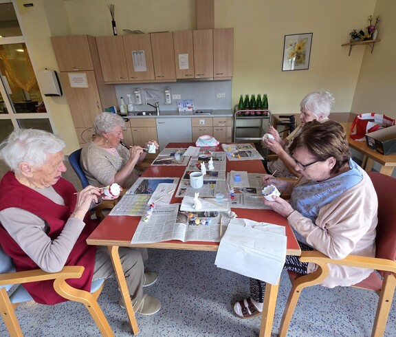 Bewohnerinnen des Pflegewohnhauses bemalen gemeinsam Keramikfiguren und gestalten farbenfrohe Osterdekorationen an einem Arbeitstisch.