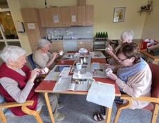 Bewohnerinnen des Pflegewohnhauses bemalen gemeinsam Keramikfiguren und gestalten farbenfrohe Osterdekorationen an einem Arbeitstisch.