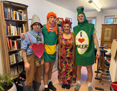 Vier verkleidete Mitarbeitende posieren gemeinsam in einem Zimmer mit Bücherregal und Deko.