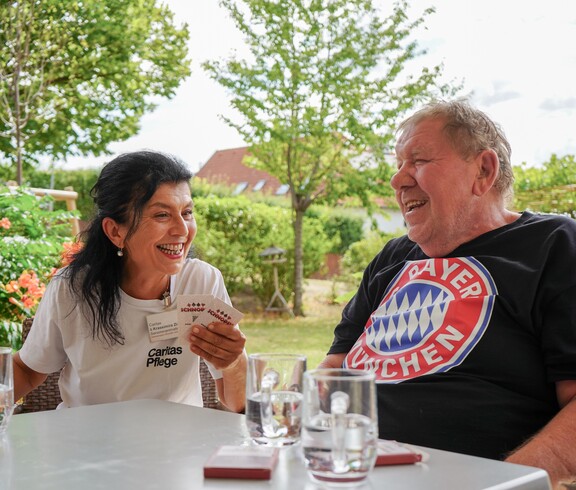 Ein Mann und eine Pflegerin spielen ein Spiel und lachen herzhaft.