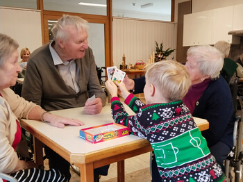 Kind zeigt Spielkarten einer Gruppe von Senior*innen am Tisch