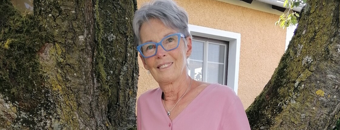 Eine Frau steht im Freien an einen Baum gelehnt und lächelt.