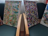 Mehrere bunt gestaltete Leinwände mit vielen Farbtupfern und abstrakten Mustern stehen nebeneinander und zeigen kreative Malarbeiten aus dem Alltag im Pflegewohnhaus.