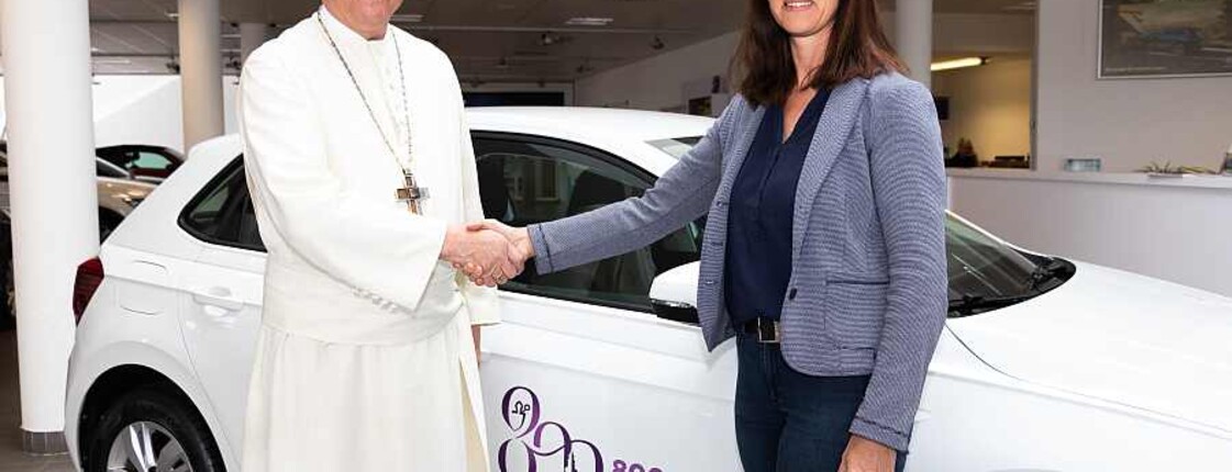 Ein Abt und eine Frau stehen vor dem neuen Auto und reichen sich die Hände