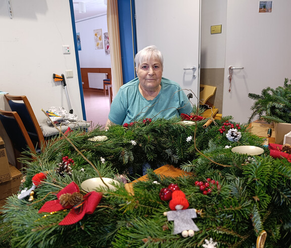 Großer Adventkranz mit roten Schleifen, Zapfen und kleinen Figuren auf Tisch
