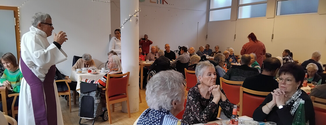 Pfarrer spricht vor Bewohner*innen im festlich dekorierten Speisesaal