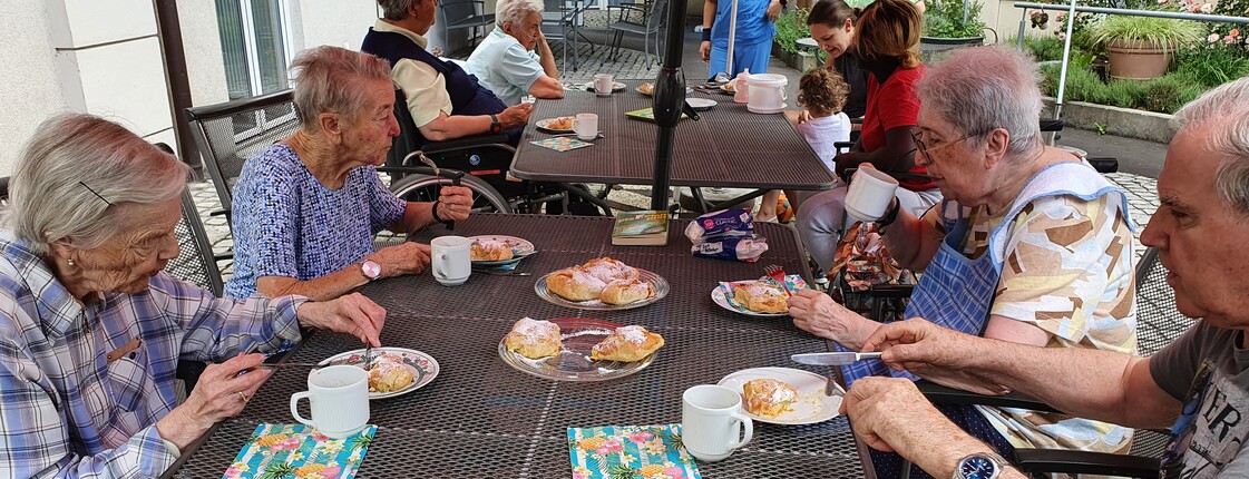 Mehrere Senior*innen sitzen am Tisch im Garten bei Kaffee und Kuchen