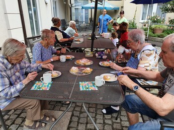 Mehrere Senior*innen sitzen am Tisch im Garten bei Kaffee und Kuchen
