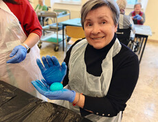 Bewohnerin färbt Ostereier mit Farben und Handschuhen im Gemeinschaftsraum.