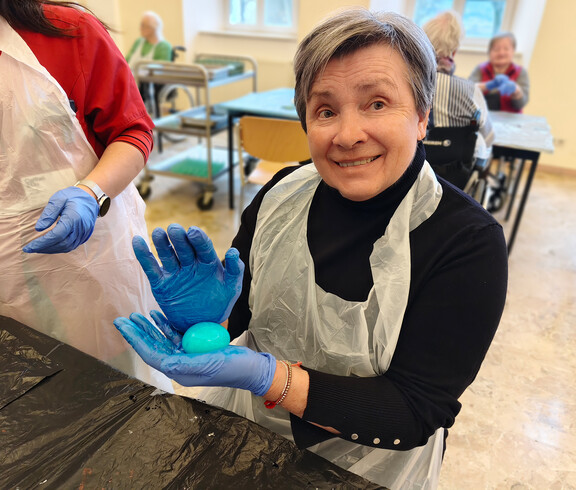 Bewohnerin färbt Ostereier mit Farben und Handschuhen im Gemeinschaftsraum.