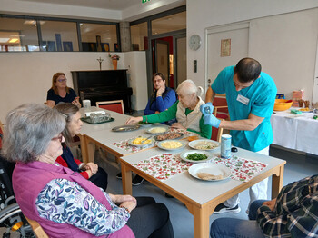 Ein Praktikant unterstützt eine Seniorin bei der Zubereitung eines tunesischen Gerichts am Tisch.