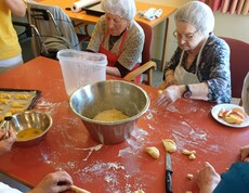 Bewohnerinnen des Pflegewohnhauses bereiten gemeinsam frischen Germteig vor. Am großen Tisch wird geknetet, geformt und gelacht, während verschiedene Teigstücke für das Backblech entstehen.