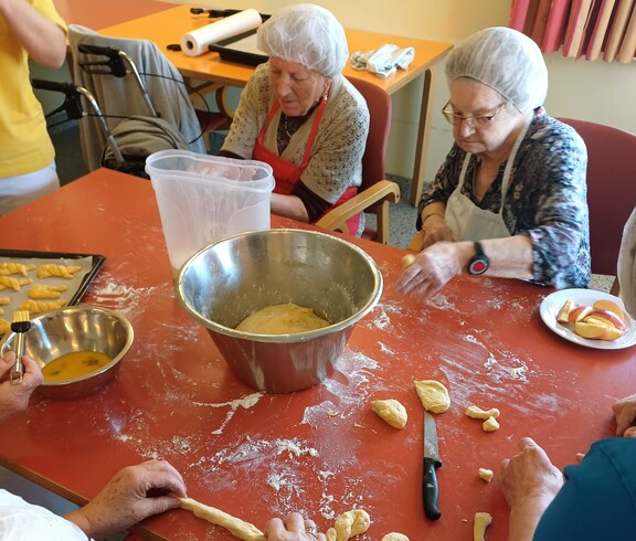 Bewohnerinnen des Pflegewohnhauses bereiten gemeinsam frischen Germteig vor. Am großen Tisch wird geknetet, geformt und gelacht, während verschiedene Teigstücke für das Backblech entstehen.