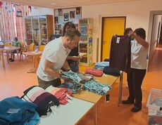 Mehrere Personen bereiten im Gemeinschaftsraum des Pflegewohnhauses Kleidung auf Tischen für eine Modeschau vor.