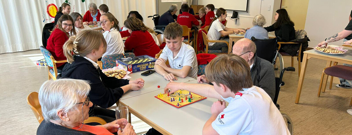 Mehrere Gruppen aus Jugendlichen und Bewohner*innen spielen Brettspiele an verschiedenen Tischen.