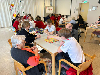 Mehrere Gruppen aus Jugendlichen und Bewohner*innen spielen Brettspiele an verschiedenen Tischen.