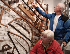 Besucher*in im Rollstuhl betrachtet mit Begleiter alte Holzwerkzeuge an einer Ausstellungswand