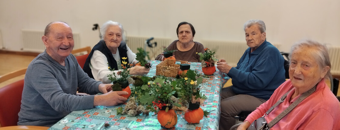Bewohner*innen gestalten mit Naturmaterialien herbstliche Dekorationen an einem gemeinsamen Tisch.