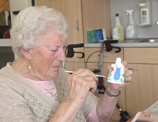 Eine Bewohnerin des Pflegewohnhauses gestaltet aufmerksam eine bunte Keramikfigur. Auf dem Tisch liegen Zeitungen als Unterlage sowie Pinsel und Farben. Die kreative Tätigkeit findet in einem der Gemeinschaftsräume statt.