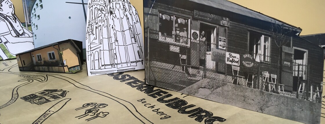 Aus Papier ausgeschnittene Gebäude stehen auf einer von Hand gezeichneten Karte.