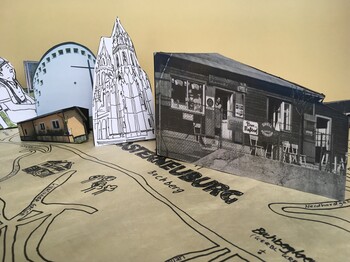 Aus Papier ausgeschnittene Gebäude stehen auf einer von Hand gezeichneten Karte.