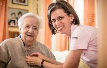 Eine Caritas Mitarbeiterin knöpft einer Klientin die Bluse zu.