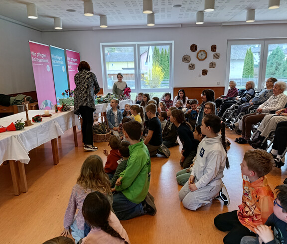 Bewohner*innen und Kinder nehmen gemeinsam an einer Osterandacht im Gemeinschaftsraum teil.