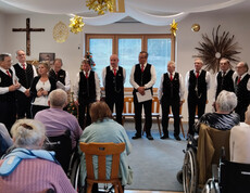 Gruppe von Sänger*innen vor Publikum, festlich gekleidete Gäste hören zu