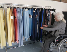 Bewohnerin im Rollstuhl betrachtet Hosen in vielen Farben an einem Kleiderständer