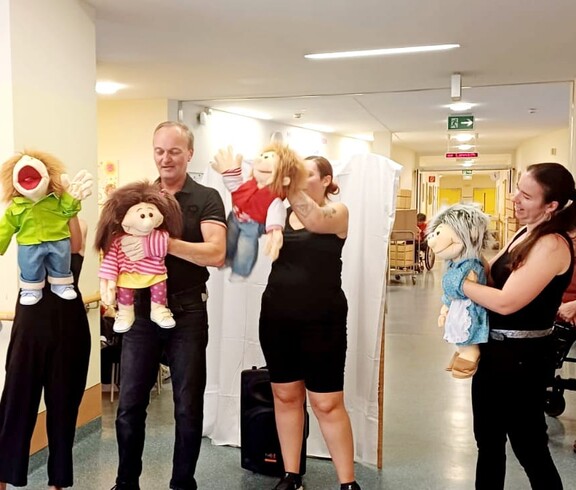 Vier schwarz gekleidete Puppenspieler stehen vor den Bewohner*innen des Caritas Pflegewohnhauses Lannach und führen eine Puppenshow auf. Die Szene zeigt eine lebendige Unterhaltung im Pflegealltag.