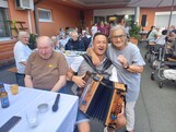 Eine Person mit einer Ziehharmonika sitzt zwischen den Gästen des Sommerfestes, während die Bewohnerinnen und Bewohner an festlich gedeckten Tischen im Innenhof zusammensitzen und der Musik lauschen.