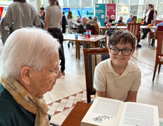 Eine Schüler liest einer Bewohnerin aus einem aufgeschlagenen Buch beim österreichischen Vorlesetag im Haus Suavitas vor.