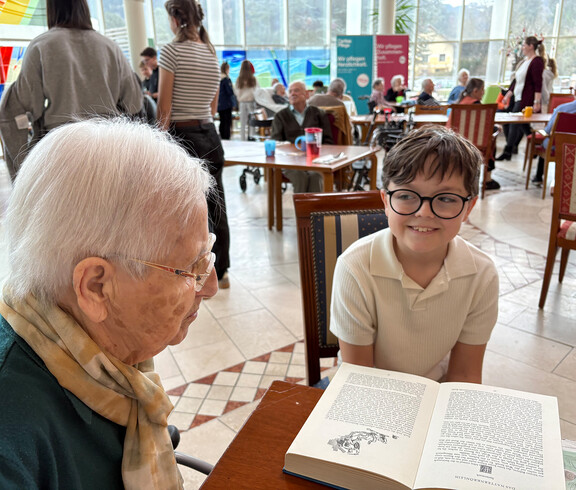 Eine Schüler liest einer Bewohnerin aus einem aufgeschlagenen Buch beim österreichischen Vorlesetag im Haus Suavitas vor.