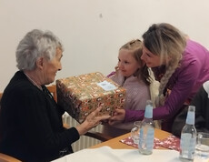 Bewohner*in erhält ein verpacktes Geschenk von einem Mädchen, begleitet von einer Erwachsenen.