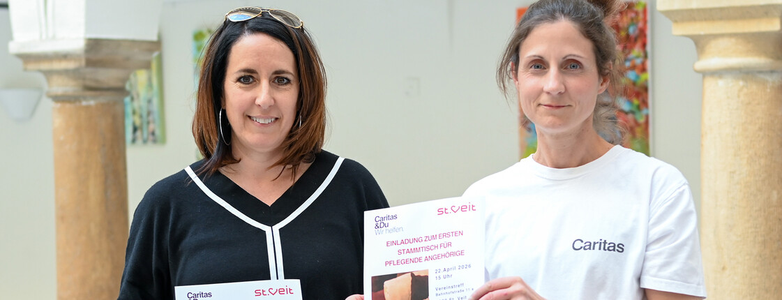 Frau Greiler von der Stadt St.Veit und Verena Wernbacher von der RegionalCaritas halten Flyer zum Pflegestammtisch für pflegende Angehörige in St. Veit.