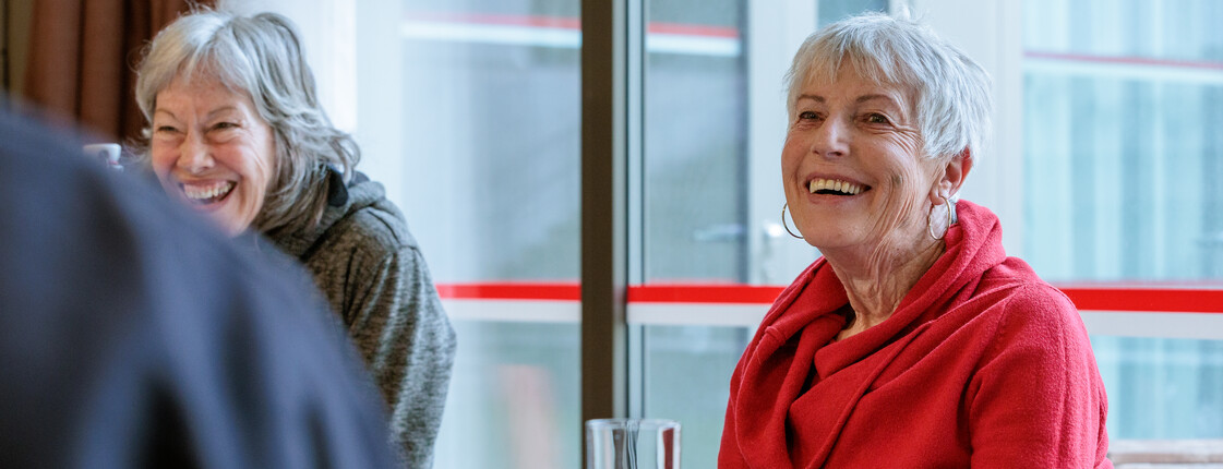 Bei einer Gesprächsrunde für pflegende Angehörige lachen zwei Frauen ausgelassen.