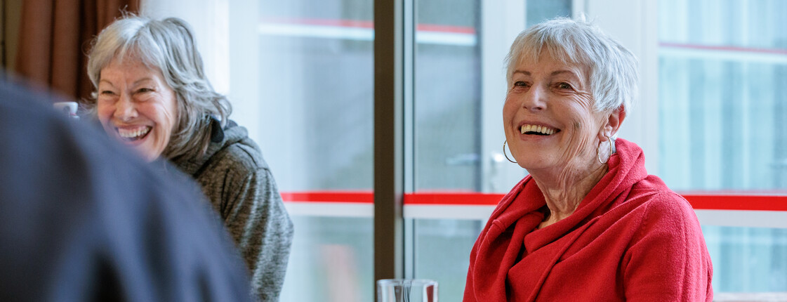 Bei einer Gesprächsrunde für pflegende Angehörige lachen zwei Frauen ausgelassen.