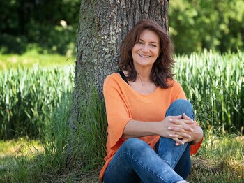 Andra Fuchst sitzt in der Wiese vor einem Baum
